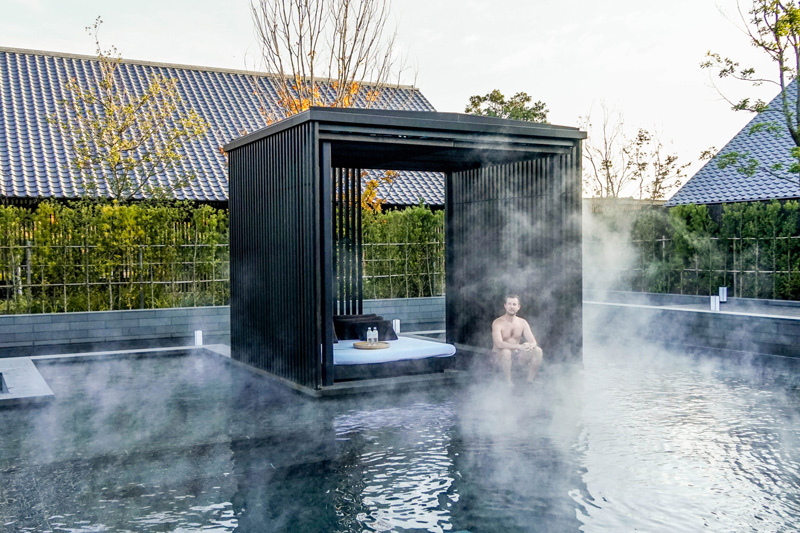 Person relaxing in an open-air onsen pavilion surrounded by steam