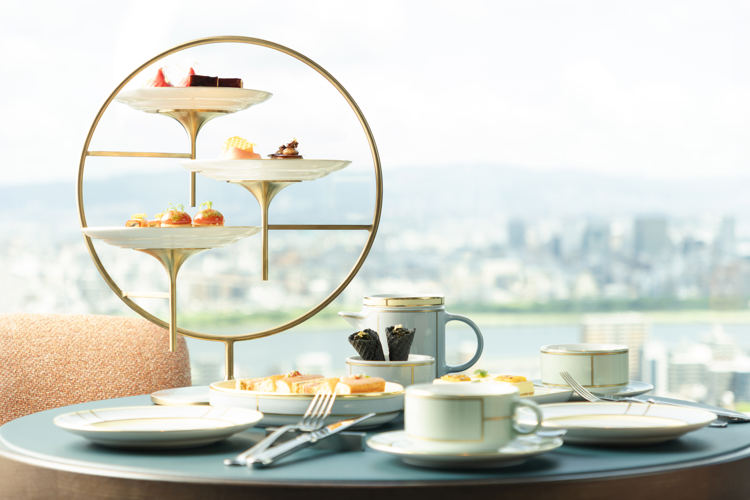 Tiered afternoon tea stand with pastries in front of a hazy city skyline view