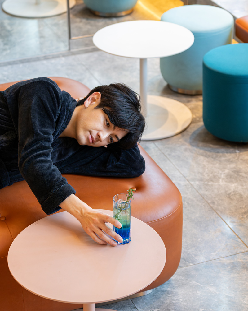 Guest reclining on a lounge sofa reaching for a cocktail on a low round table